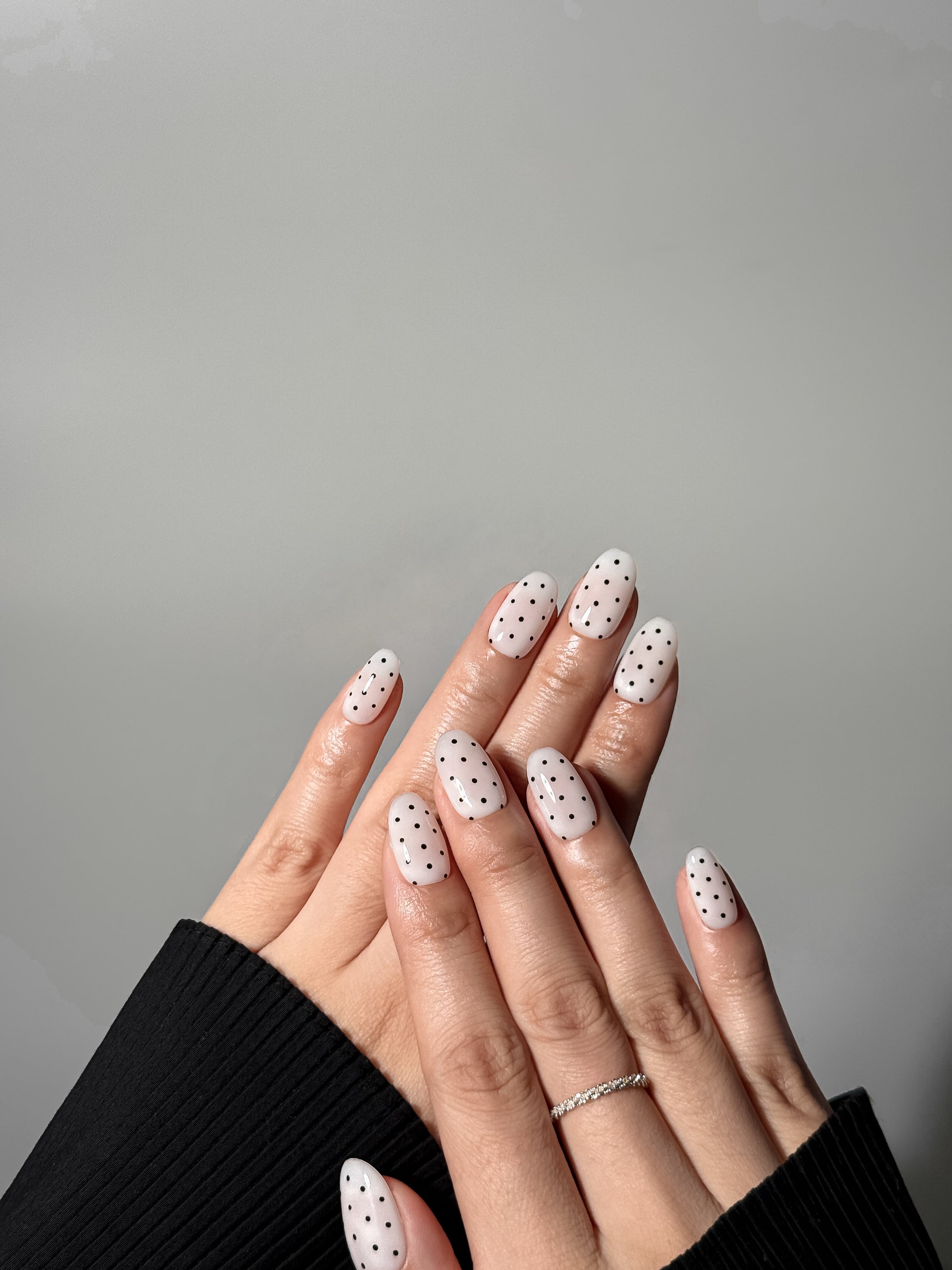 Hands displayed together showing a full monochrome manicure of white nails with black dots, styled with a silver eternity band.