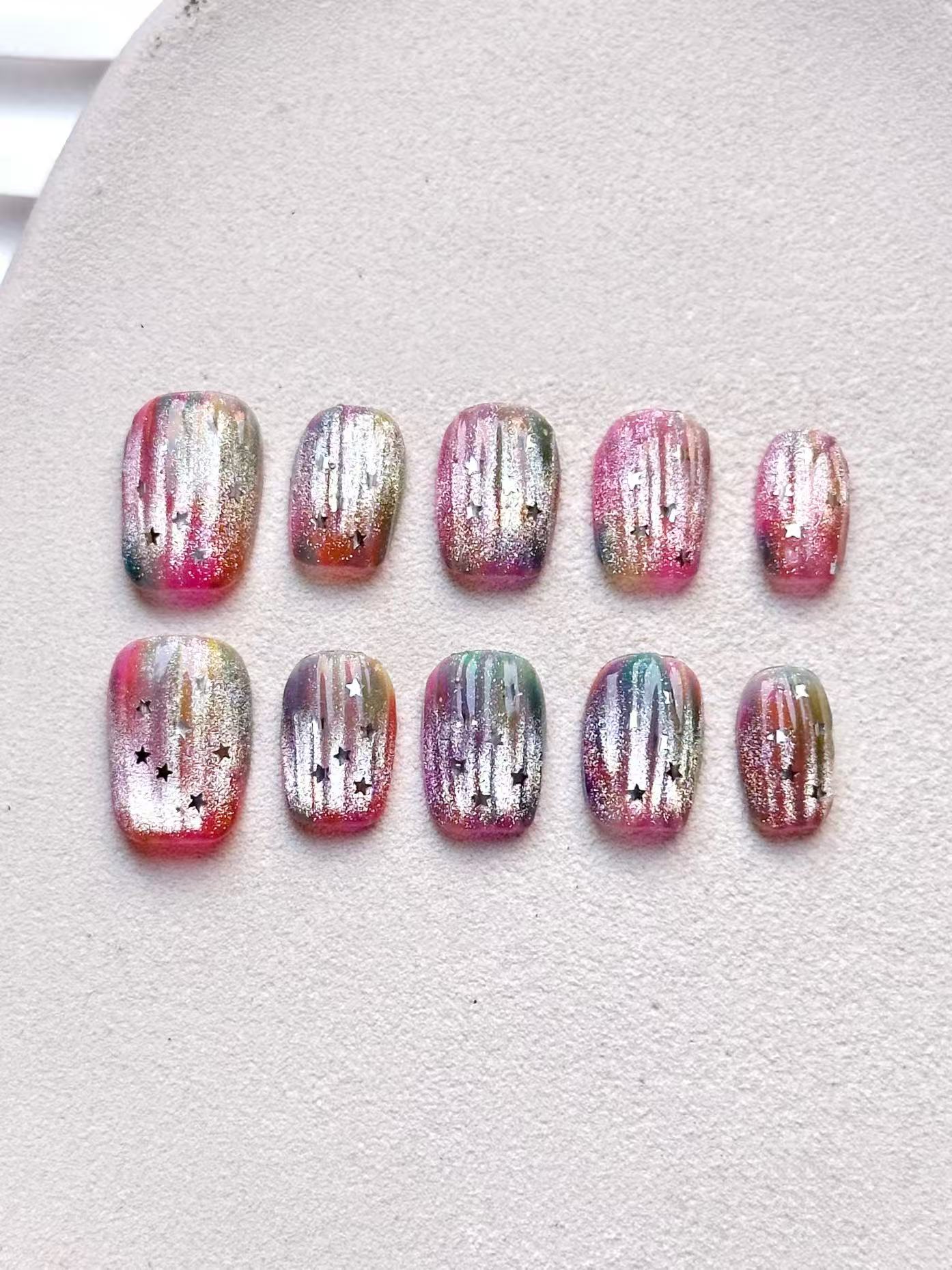 A flat lay photograph displaying all ten nails in the cosmic pink rainbow jelly star press-on nail set, arranged neatly on a surface.