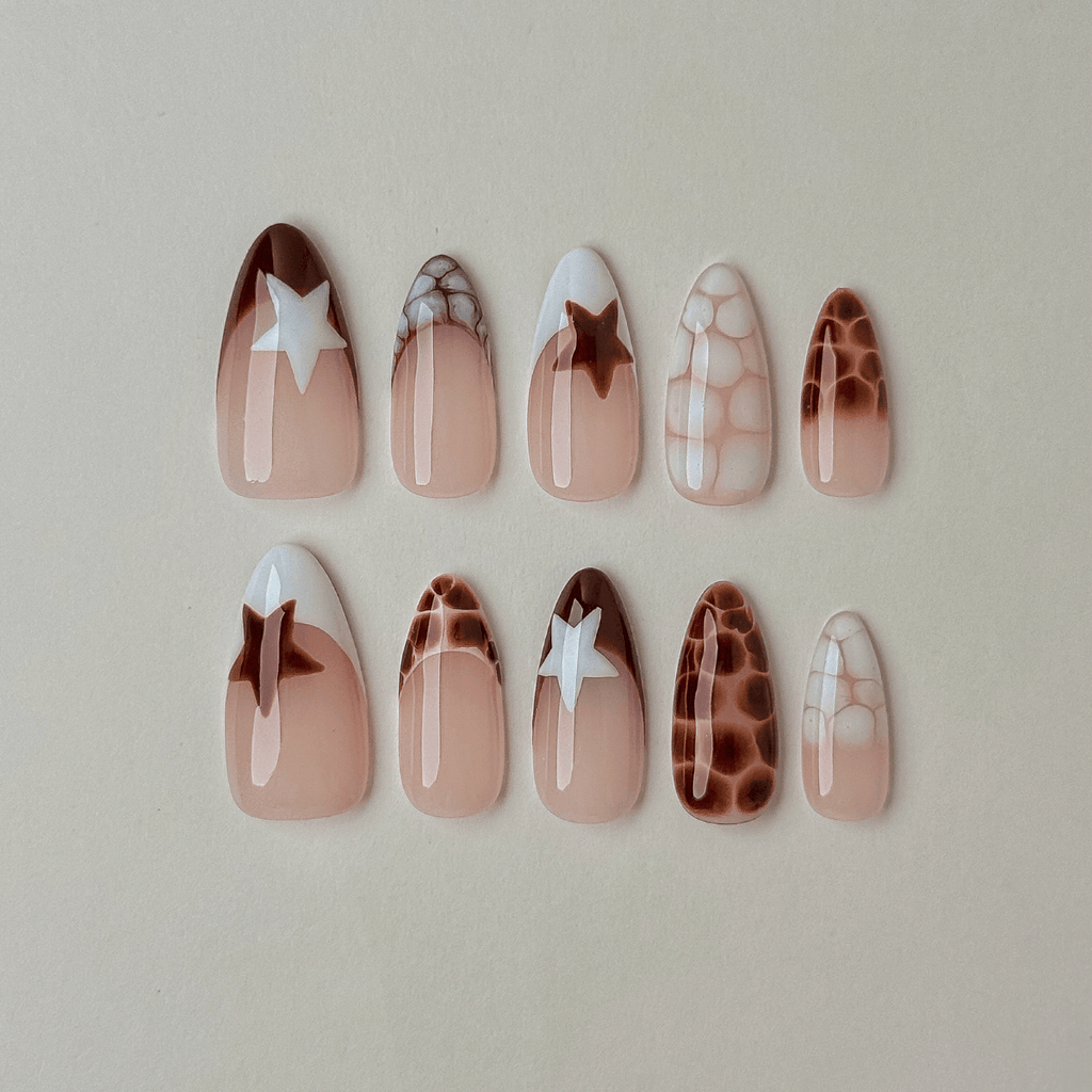 Handcrafted almond press-on nails with brown and white crocodile texture patterns and star accent French tips laid flat on a gray background.
