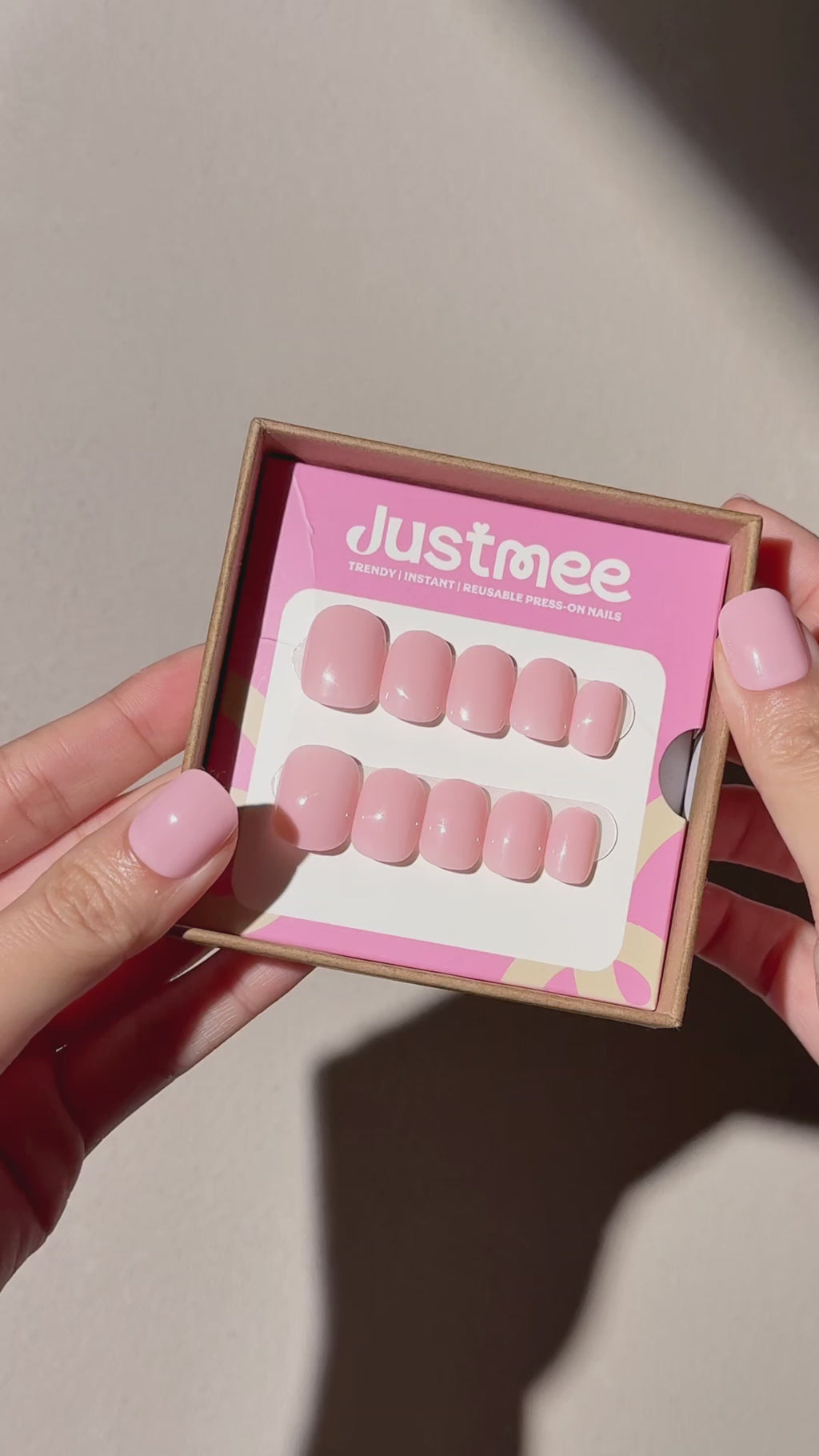 2 hands showing Justmee press-on nails in the package, and one hand shows the nails in soft pink color in short square shape, featuring the most trendy milkshake clean girl style in 2026