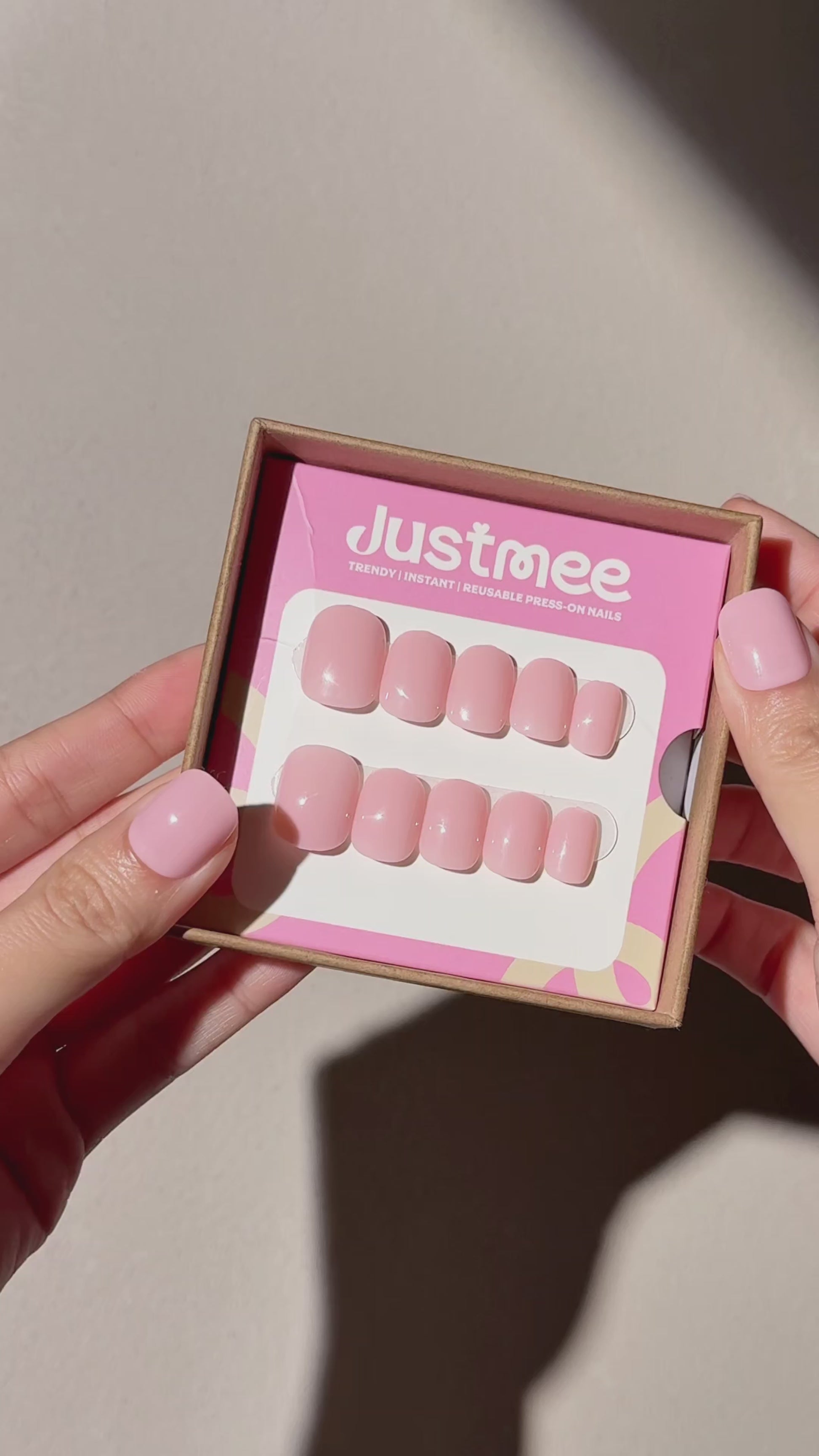 2 hands showing Justmee press-on nails in the package, and one hand shows the nails in soft pink color in short square shape, featuring the most trendy milkshake clean girl style in 2026