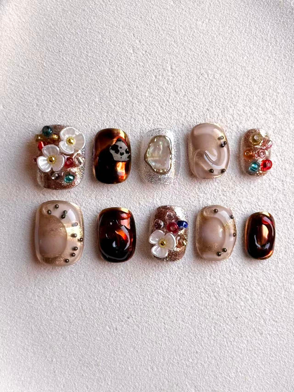Overhead view of designer press-on nails with iridescent shell inlay and amber marble texture