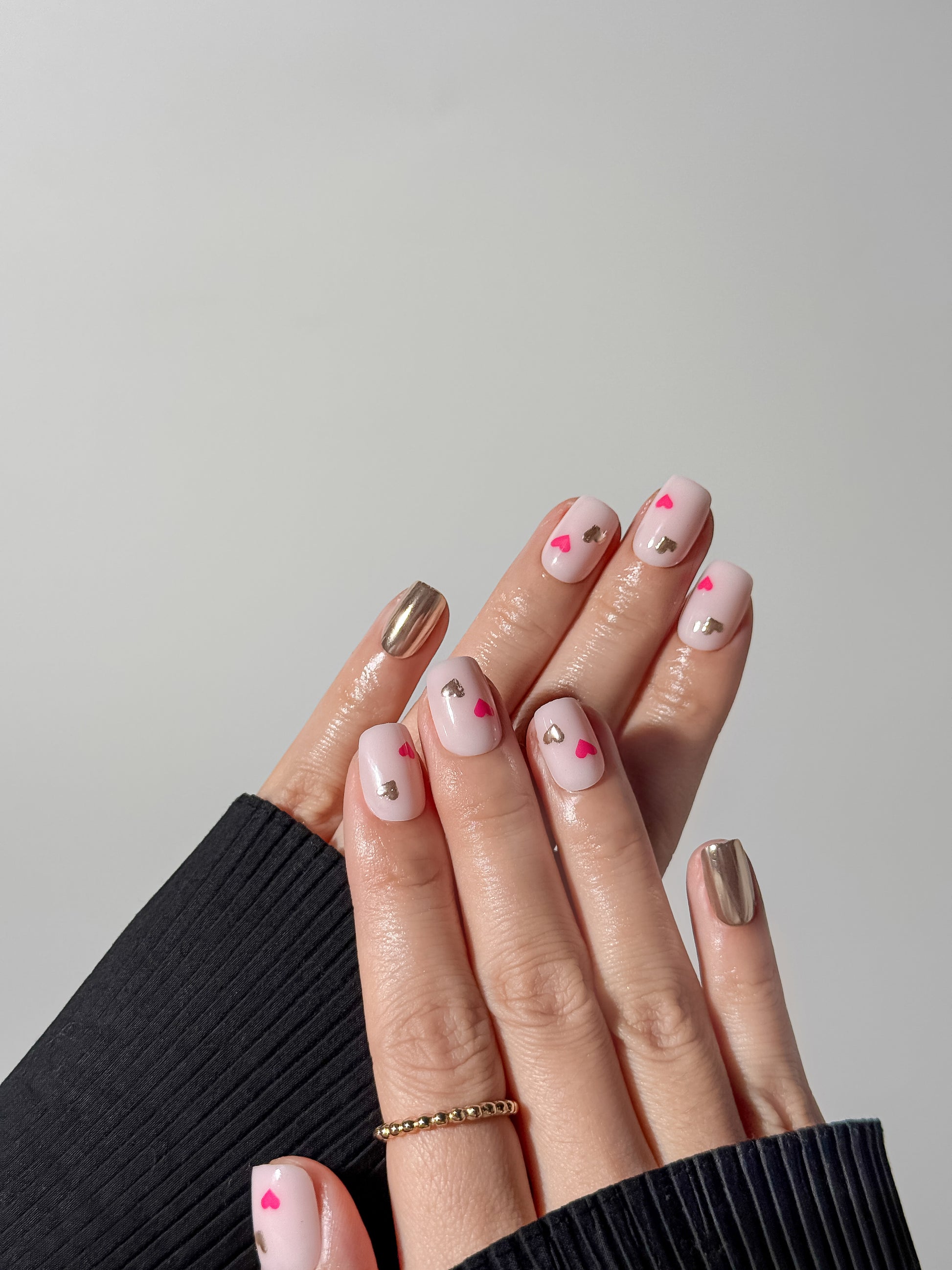 Minimalist heart-themed press-on nails with silver chrome accent nail, styled with gold rings and black clothing