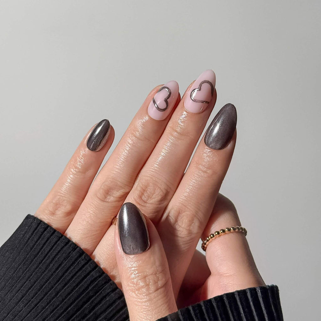 Close-up of a metallic heart-themed manicure with graphite chrome accents styled with gold rings.