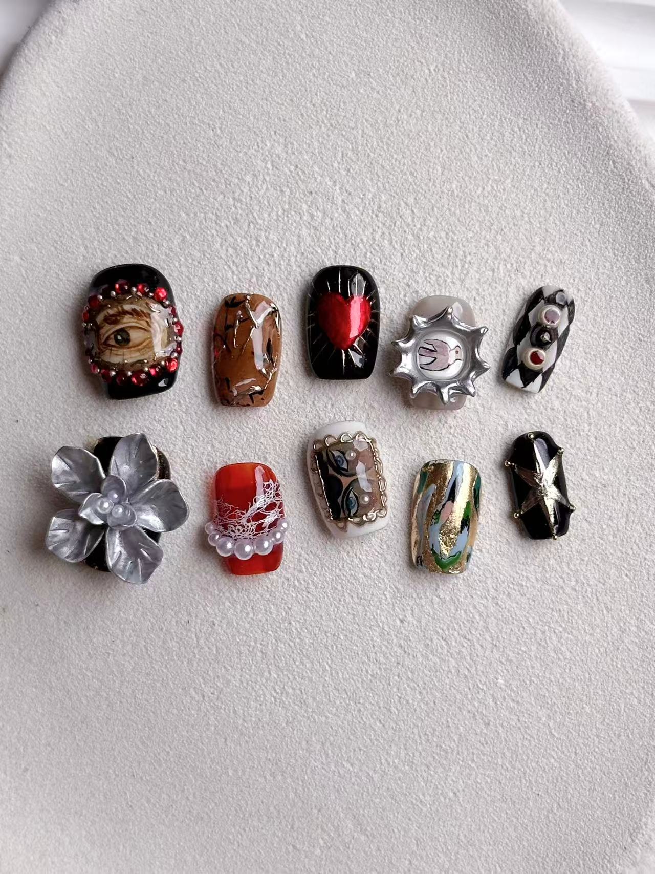 Flatlay of a 10-piece luxury nail set with eclectic surrealist designs and architectural 3D accents.