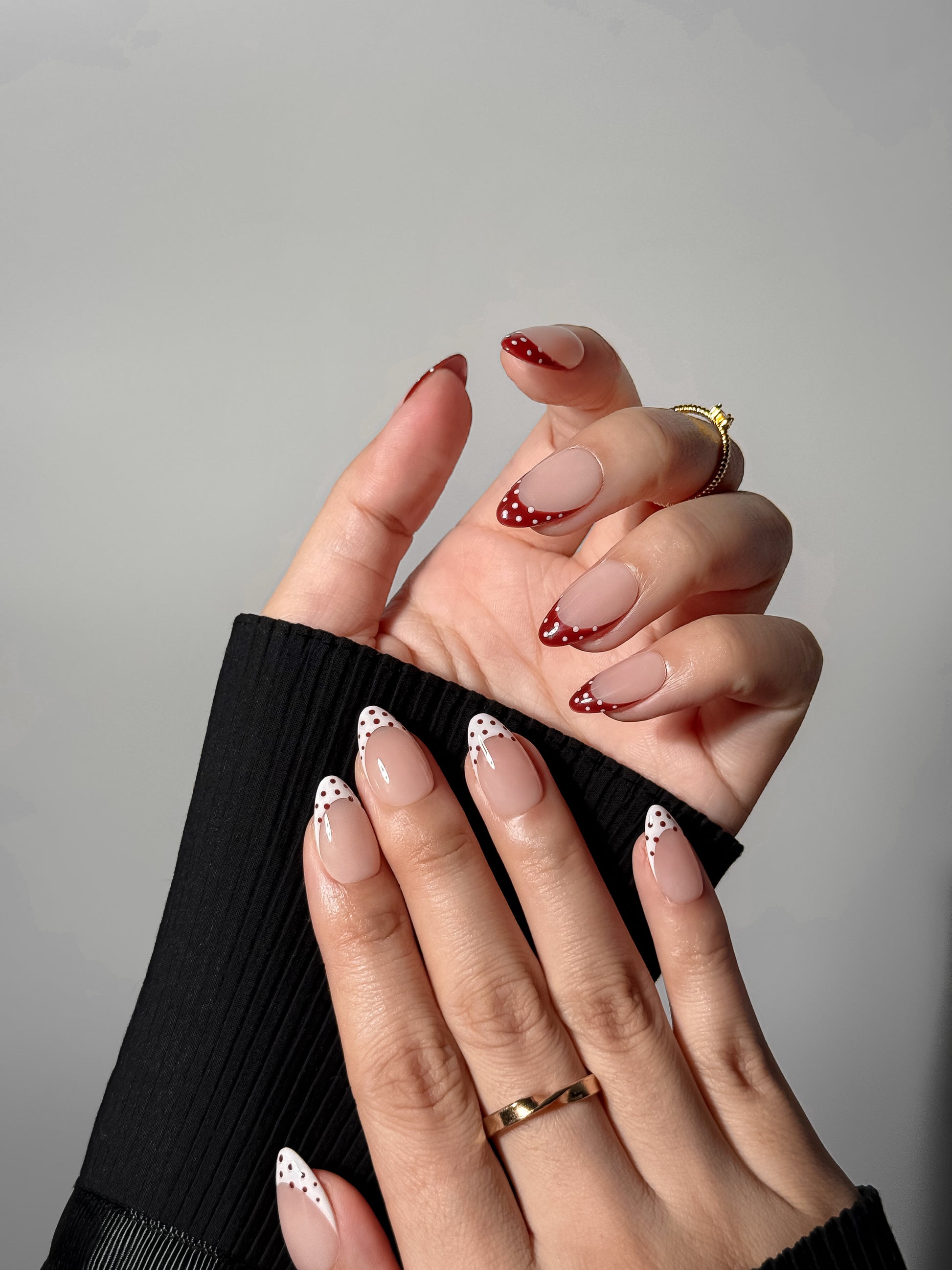 A stylized pose showing a hand with red and white dotted French tip nails, highlighting a modern and feminine "coquette" aesthetic.