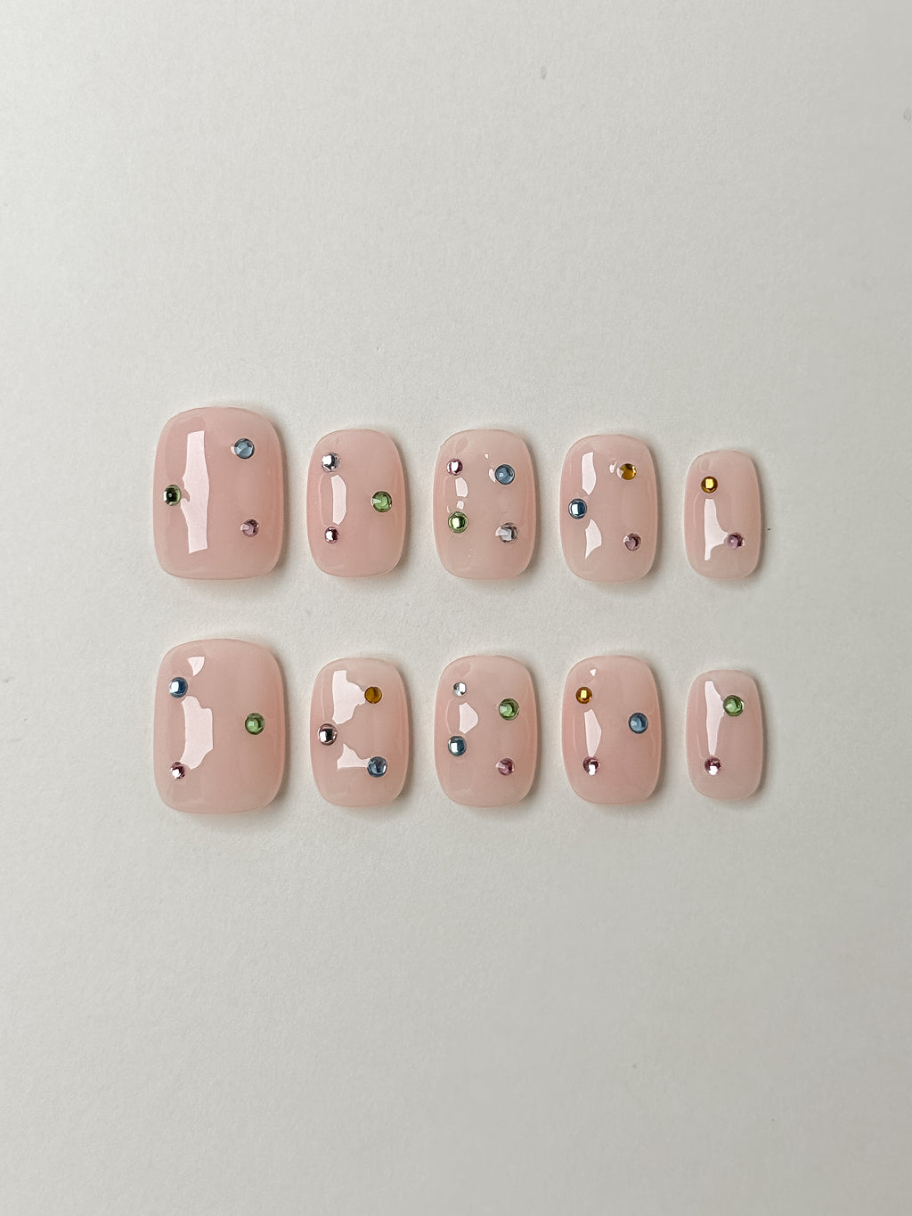 Flat lay of Twinkle Pop short square nude press-on nails with colorful gem accents – Justmee